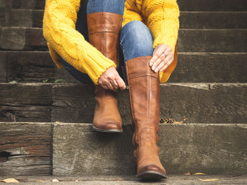 Woman sitting on stairs and fasten zipper on her leather boots. Autumn fashion concept